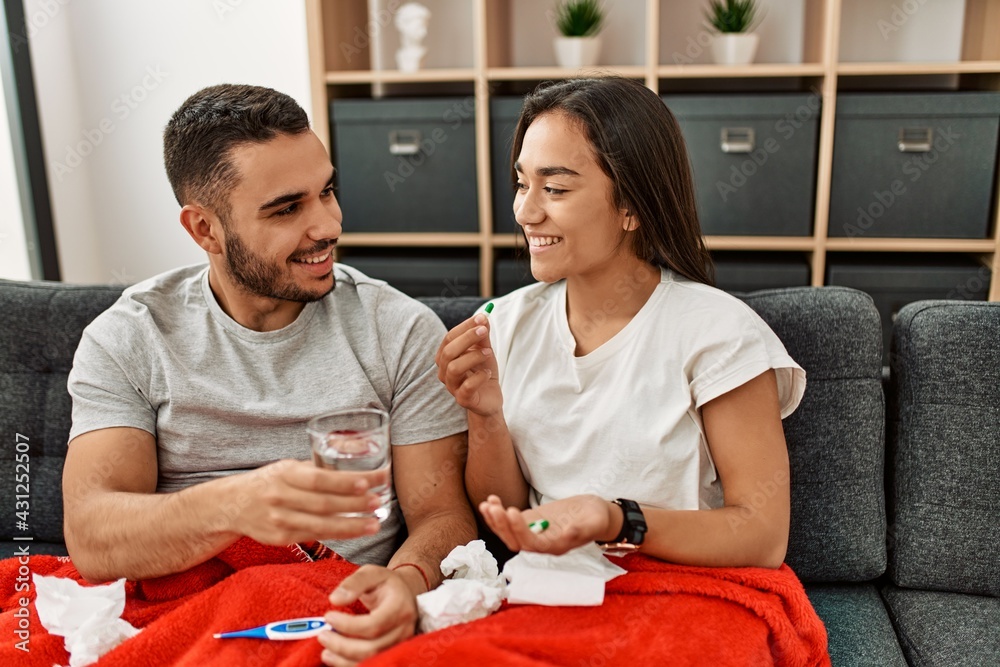 Fototapeta premium Young latin ill couple eating pills sitting on the sofa at home.