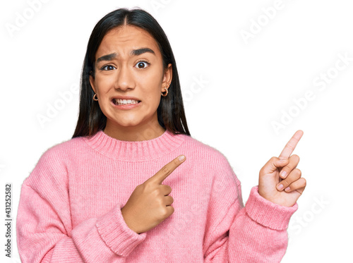 Young asian woman wearing casual winter sweater pointing aside worried and nervous with both hands  concerned and surprised expression