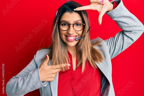 Beautiful brunette woman working at the office wearing operator headset smiling making frame with hands and fingers with happy face. creativity and photography concept.