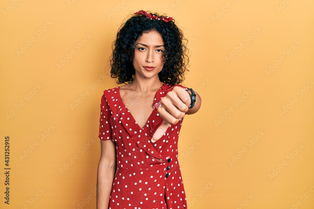 Young latin girl wearing summer dress looking unhappy and angry showing rejection and negative with thumbs down gesture. bad expression. Young latin girl wearing summer dress looking unhappy and angry showing rejection and negative with thumbs down gesture. bad expression.