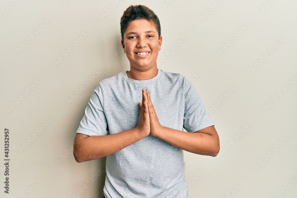 Teenager hispanic boy wearing casual grey t shirt praying with hands together asking for forgiveness smiling confident. Teenager hispanic boy wearing casual grey t shirt praying with hands together asking for forgiveness smiling confident.