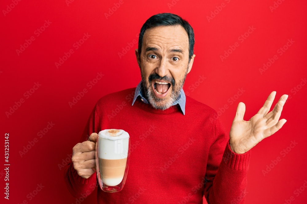 Middle age hispanic man drinking a cup of cappuccino coffee celebrating victory with happy smile and winner expression with raised hands Middle age hispanic man drinking a cup of cappuccino coffee celebrating victory with happy smile and winner expression with raised hands