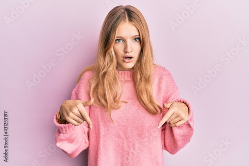 Beautiful young caucasian girl wearing casual clothes pointing down with fingers showing advertisement  surprised face and open mouth