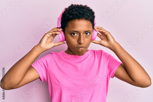 Young african american girl listening to music using headphones skeptic and nervous, frowning upset because of problem. negative person.