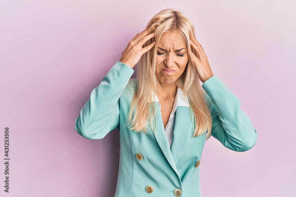 Young blonde woman wearing business clothes suffering from headache desperate and stressed because pain and migraine. hands on head. Young blonde woman wearing business clothes suffering from headache desperate and stressed because pain and migraine. hands on head.