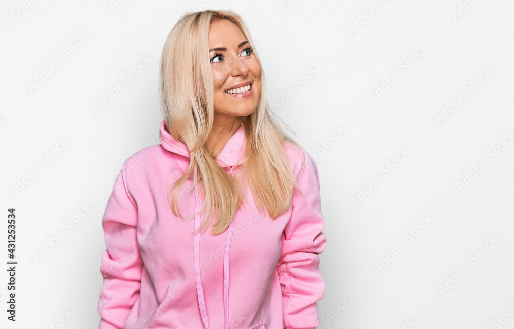 Young blonde woman wearing casual sweatshirt looking away to side with smile on face, natural expression. laughing confident. Young blonde woman wearing casual sweatshirt looking away to side with smile on face, natural expression. laughing confident.