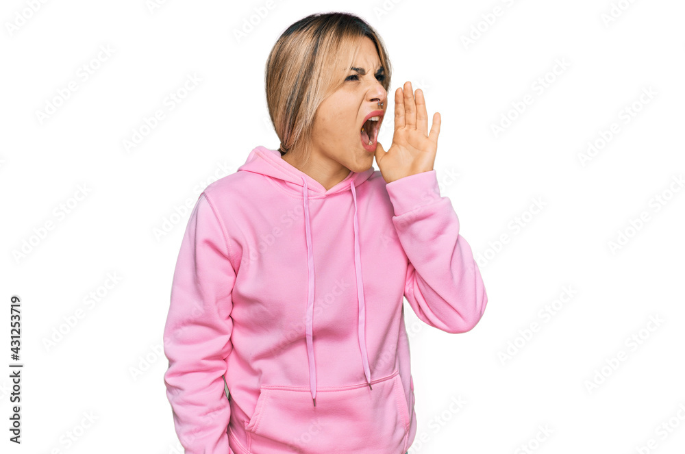 Young caucasian woman wearing casual sweatshirt shouting and screaming loud to side with hand on mouth. communication concept.
