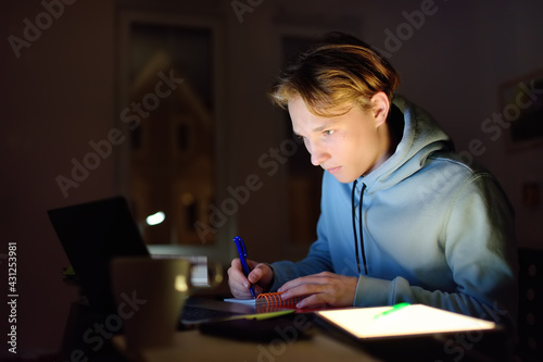 Shocked teenger studying night at home with laptop and tablet pc. Online learning, distance lessons, freelance - modern lifestyle