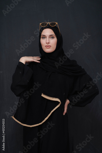 Young muslim in traditional clothes or abaya and sunglasses posing in front of black chalkboard photo