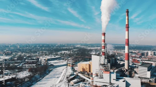 Drone footage of smoke coming out from the chimney of a thermal power plant in the industrial area of Wroclaw, Poland. Harmful smoke polluting the beautiful blue sky. City skyline.  photo