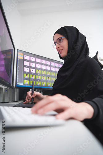 Muslim female graphic designer working on computer using graphic tablet and two monitors