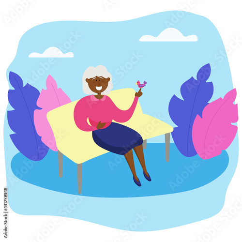 Black grandmother on a park bench with a bird. An elderly woman spends time outdoors.