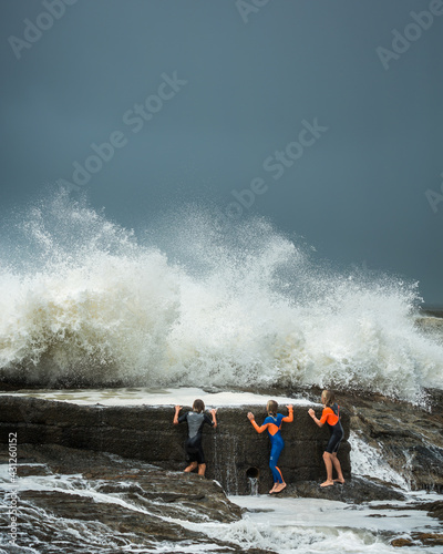 people hiding behind the barrel wall as large waves crash over it