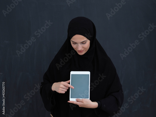 Young Arab businesswoman in traditional clothes or abaya and glasses showing tablet computer display