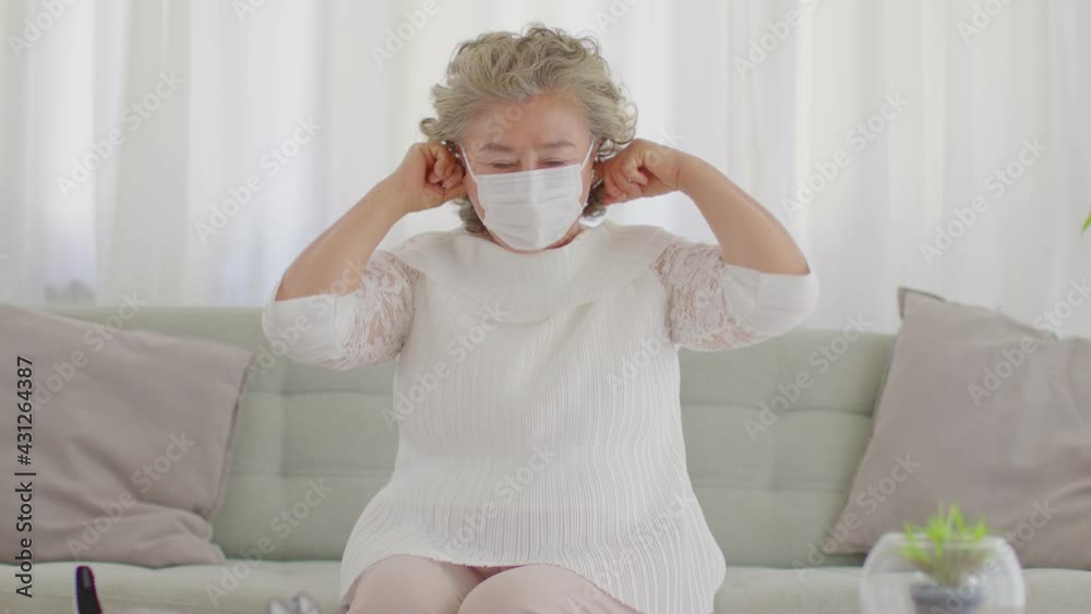 Happy Asian Elderly or Seniors woman wearing medical mask to prevent coronavirus cross arms sitting on sofa in living room at home,New normal lifestyle of older stay at home Happy Asian Elderly or Seniors woman wearing medical mask to prevent coronavirus cross arms sitting on sofa in living room at home,New normal lifestyle of older stay at home
