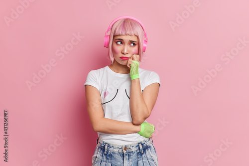 Obraz na plátně Dejected displeased Asian woman has unhappy expression keeps hand on cheek wears