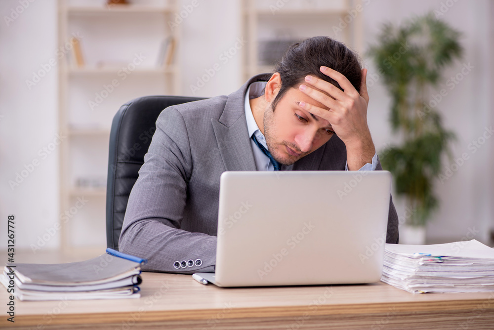 Young male employee unhappy with excessive work in the office Young male employee unhappy with excessive work in the office