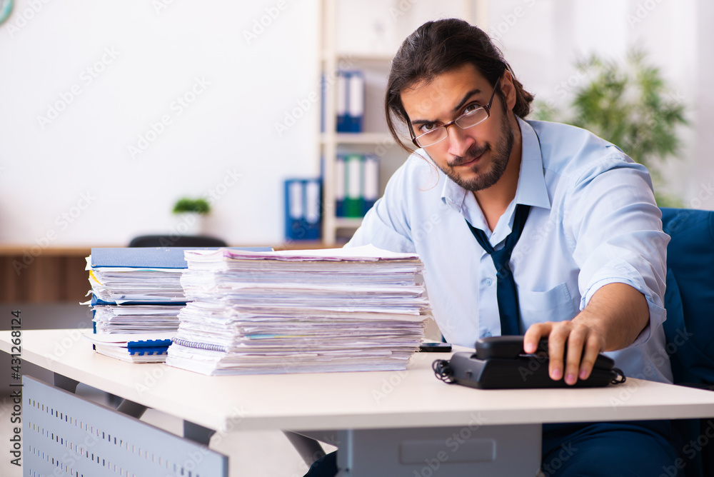 Young male employee unhappy with excessive work in the office Young male employee unhappy with excessive work in the office