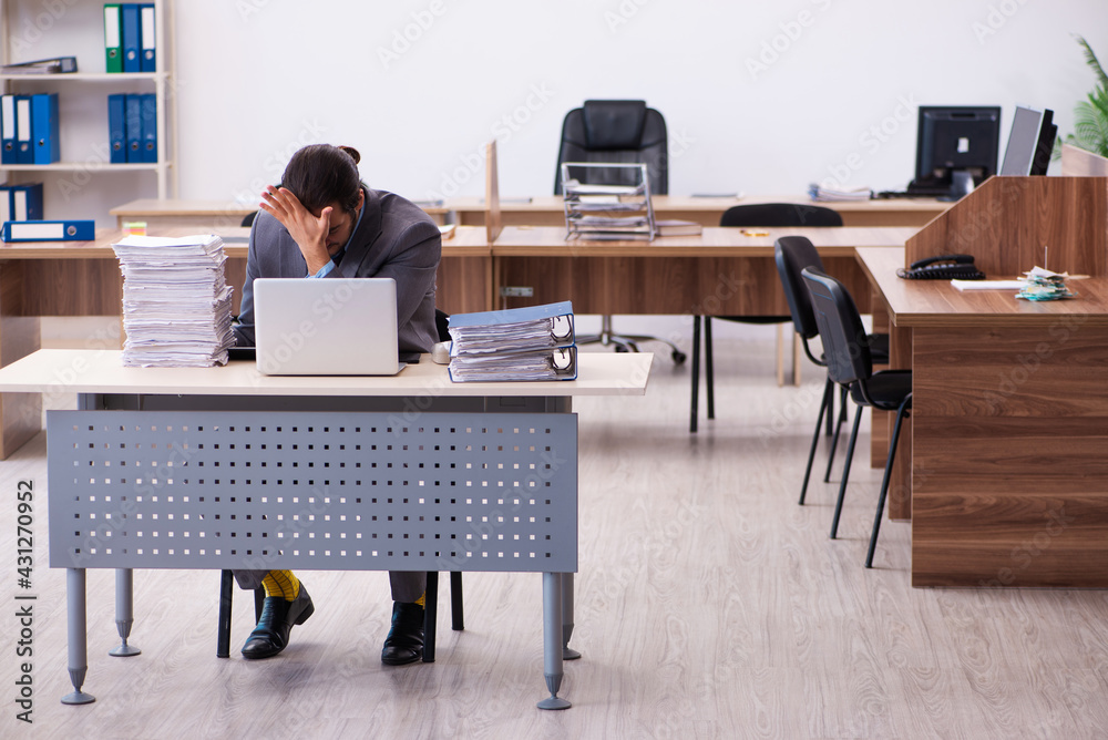 Fototapeta premium Young male employee unhappy with excessive work in the office