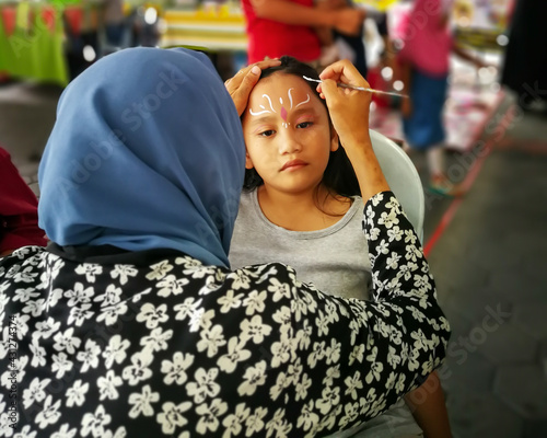 Children face painting. Artist painting little girl at the shop. photo