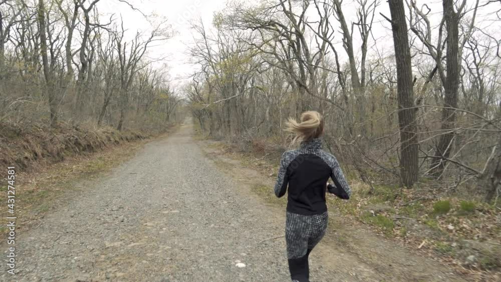Sports running. Close-up. Back view. A young girl with long hair runs along an empty forest road. The camera moves to a female triathlon athlete in the woods.