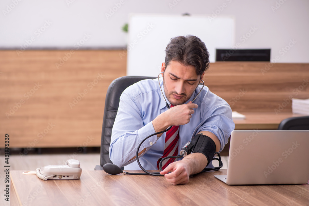 Young male employee suffering from hypertension at workplace