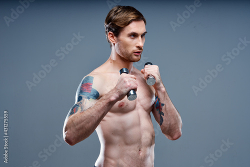 guy with a pumped up torso and with dumbbells on a gray background cropped view of the press and biceps fitness