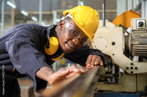 Professional African American engineer or worker wearing a hard hat and measuring the piece of metal pipe and smiling in the factory.