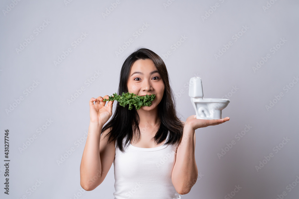 Happy asian woman with kale leaf holding a toilet model. Happy asian woman with kale leaf holding a toilet model.