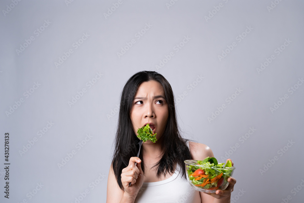 Fototapeta premium Asian woman confused with eating salad isolated over white background.