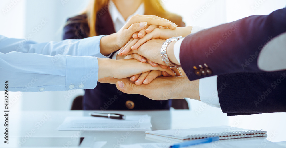 Business team showing unity with their hands together in sunny office. Group of people joining hands and representing concept of friendship and teamwork