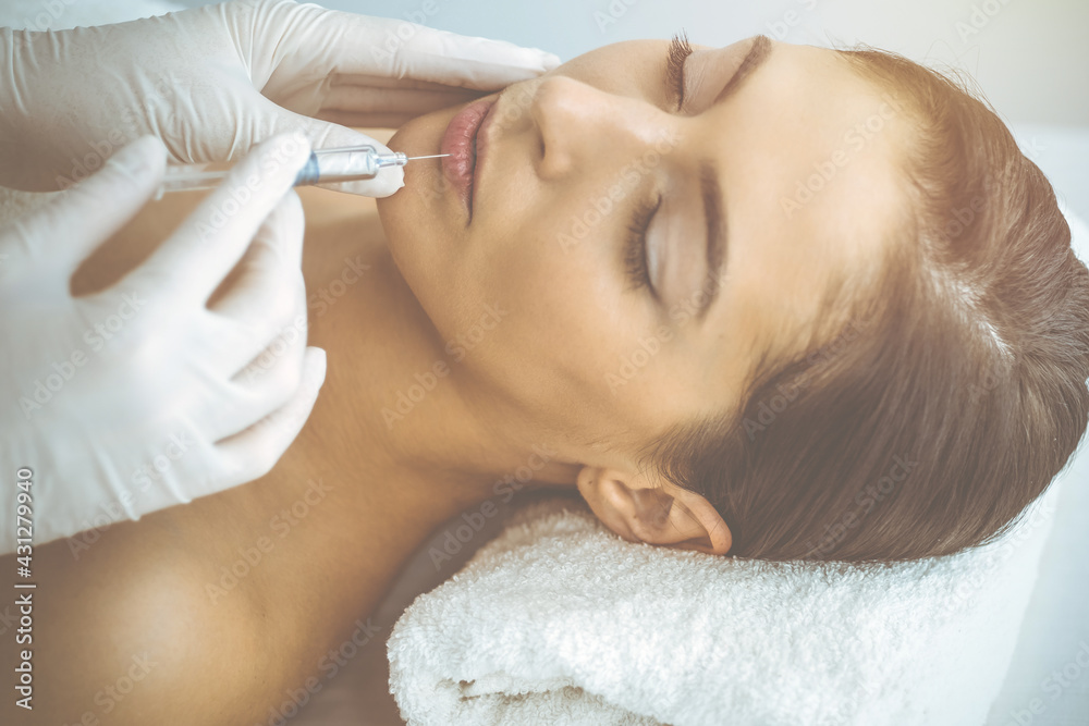 Beautician doing beauty procedure with syringe to face of young brunette woman in sunny clinic. Cosmetic medicine and surgery, beauty injections