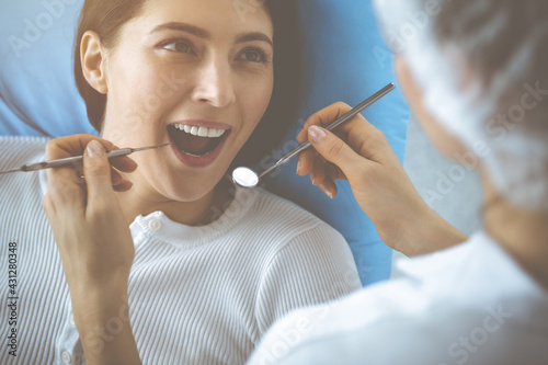 Smiling brunette woman being examined by dentist at dental clinic. Hands of a doctor holding dental instruments near patient s mouth. Healthy teeth and medicine concept