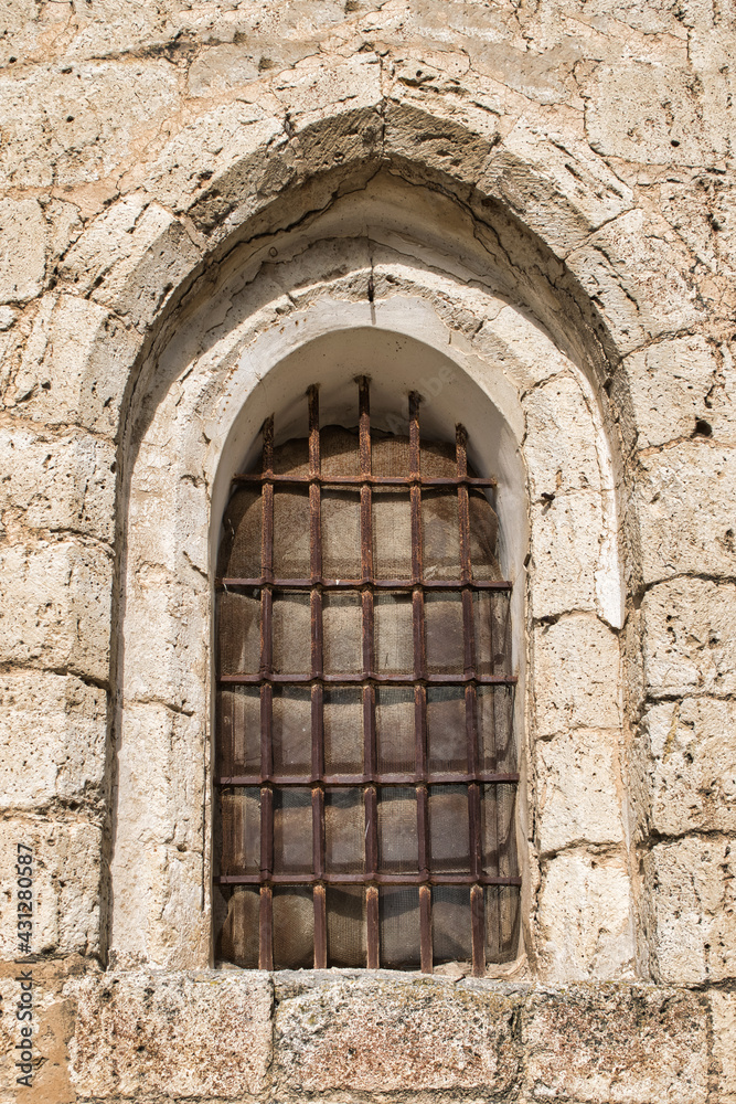 Ventana en arco apuntado de estilo románico siglo XII con barrotes de hierro en la iglesia Santiago apóstol de Villalba de los Alcores, provincia de Valladolid, España