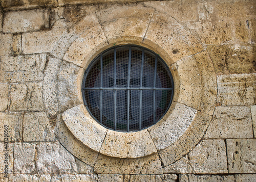 Ventana circular con barrotes de hierro en muro de piedra de la iglesia Santiago apóstol de Villalba de los Alcores, provincia de Valladolid, de estilo románico photo