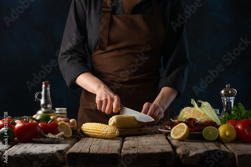 The cooking chef cuts the corn to make a dish with crayfish and potatoes. Recipe book and cooking
