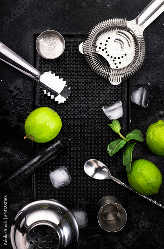 Mojito cocktail alcohol long drink making. Mint, lime, ice, white rum, cane sugar ingredients and bar utensils. Top view, white table background. Flat lay