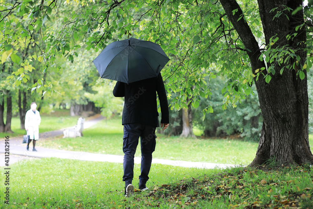 A young man in glasses walks in the park with an umbrella during the rain. A young man in glasses walks in the park with an umbrella during the rain.