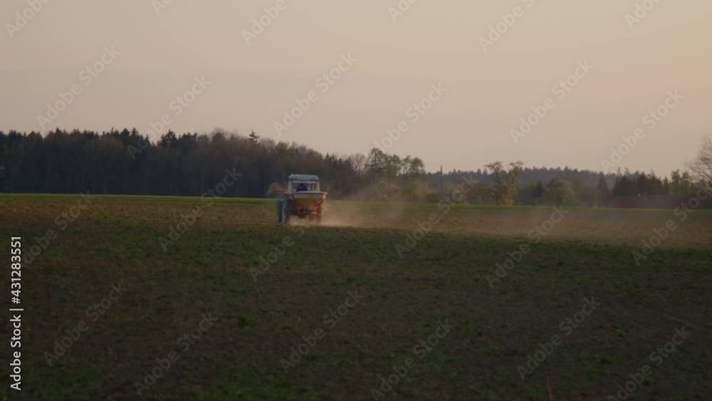 tractor distributing fertilizer on field in sunset tractor distributing fertilizer on field in sunset