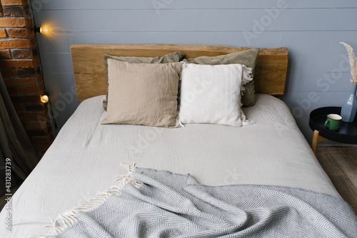 A modern Scandinavian grey bedroom with pastel-colored bedding and pillows. Wooden bed