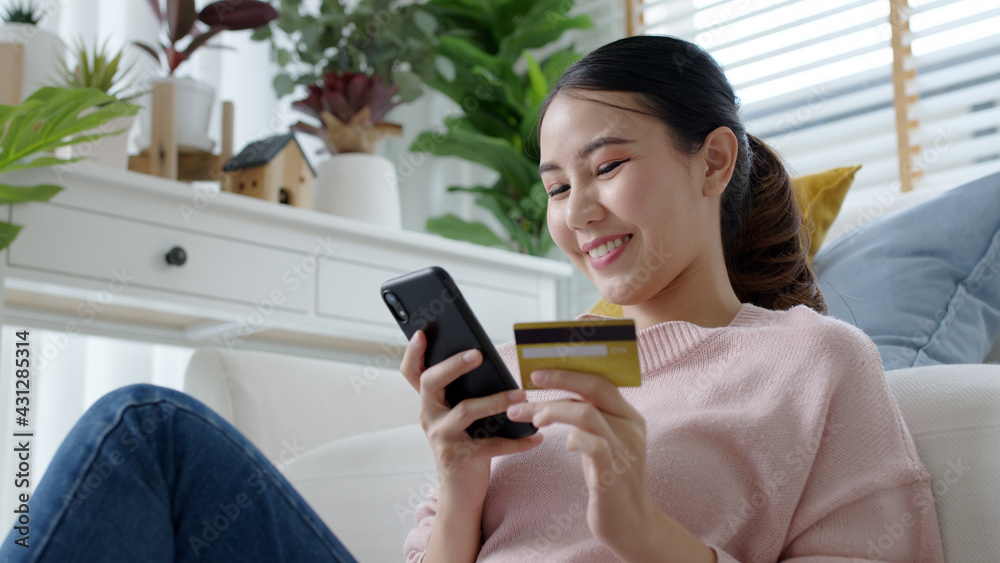 Young asian lady hold credit card in hand pay electronic money in internet online remote shopping store quarantine lifestyle at home feeling happy positive and satisfaction social distance isolate. Young asian lady hold credit card in hand pay electronic money in internet online remote shopping store quarantine lifestyle at home feeling happy positive and satisfaction social distance isolate.