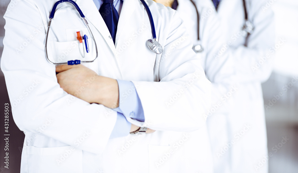 Group of modern doctors standing as a team with crossed arms and stethoscopes in hospital office. Physicians ready to examine and help patients. Medical help, insurance in health care, best desease Group of modern doctors standing as a team with crossed arms and stethoscopes in hospital office. Physicians ready to examine and help patients. Medical help, insurance in health care, best desease