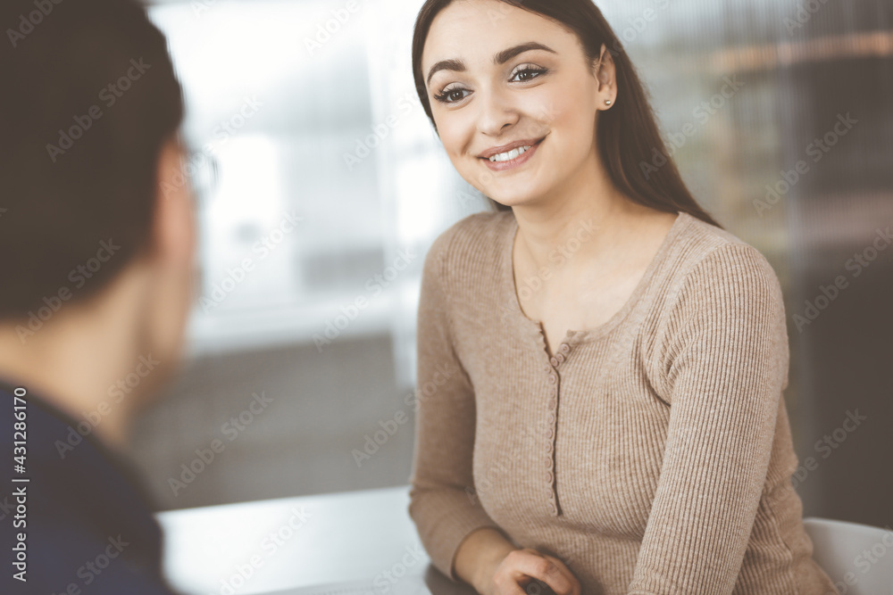 © rogerphoto - Young business people are talking to each other, while sitting at the desk in a modern office. Focus on woman. Concept of business success © rogerphoto - Young business people are talking to each other, while sitting at the desk in a modern office. Focus on woman. Concept of business success