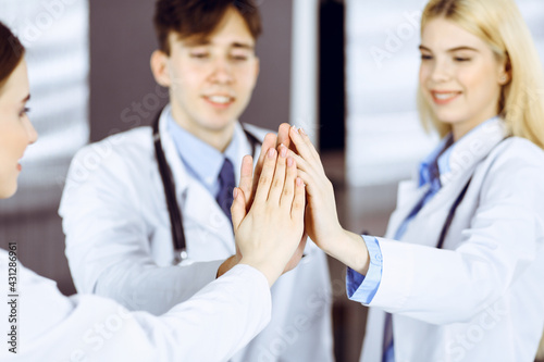 Group of modern doctors are joining hands and giving Five to each other as a sign of strong teamwork and ready to help patients. Coronavirus countering and medicine concept