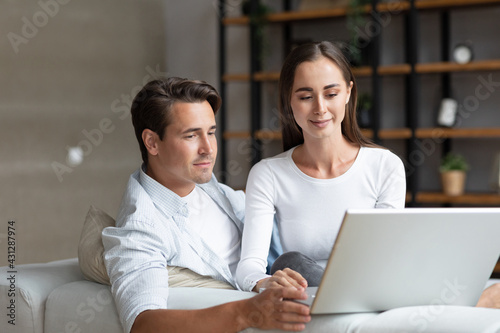 Lovely young couple using a laptop in living room at home.