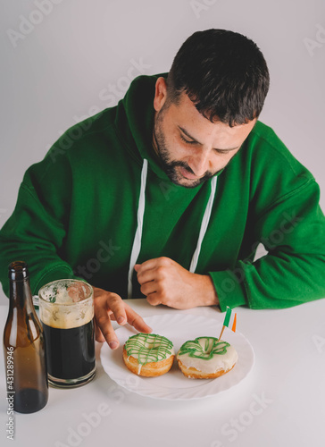 Un hombre soltero desayunando donuts con cerveza negra para celebrar el día de san patricio