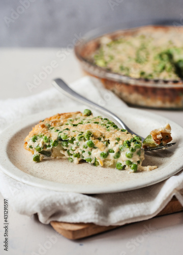 A slice of savoury pie with peas on beige plate on light-colored napkin and a whole shepherd's pie on the background