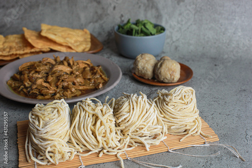 Chicken topping and raw yellow noodle displaying with meatball and green vegetable and fried dumplings