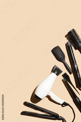 Hair brushes, hair dryer and curling wands: tools for hairdresser on pastel yellow background in hard light arranged as a side frame, a template, flat lay