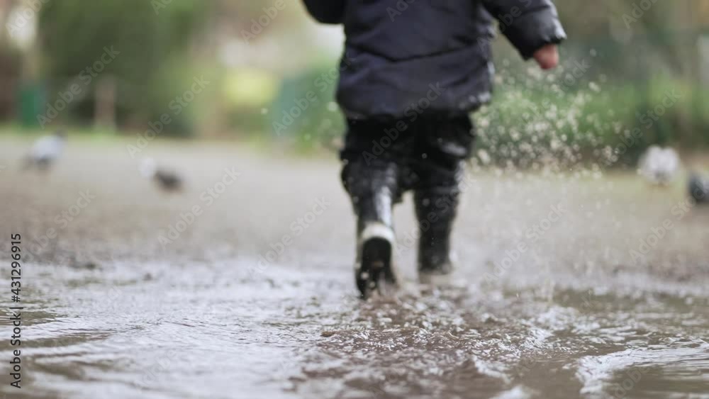 Child running in water puddle wearing rain boots